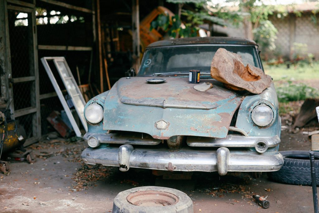 A rusty, abandoned vintage car in a workshop, surrounded by tires and tools, evoking nostalgia.