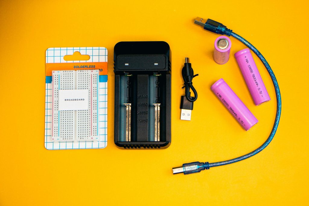 Build a New Website 2 Flat lay of electronics including a breadboard and battery charger against a vibrant yellow backdrop.